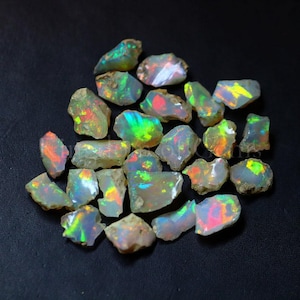 Peut inclure: Une collection de pierres d'opale brutes, chacune affichant un jeu de couleurs unique. Les opales varient en taille et en forme, avec des éclats de vert, de bleu, de rouge et de jaune. La texture rugueuse des pierres est visible sur un fond sombre.