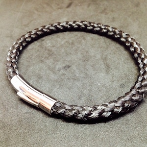 Peut inclure: Un bracelet tressé noir avec un fermoir argenté. Le bracelet est fait de cheveux et est un accessoire unique et élégant.