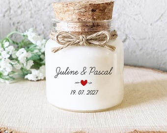 May include: A clear glass jar candle with a cork stopper and a jute twine bow tied around the neck. The front of the candle features the black printed text Juline & Pascal, a small red heart with an arrow, and the date 19. 07. 2027.