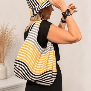 May include: A bucket hat and a hobo-style shoulder bag, both featuring a repeating pattern of vertical and horizontal stripes in mustard yellow, white, and black. The bag has a soft, unstructured shape with a wide strap for carrying over the shoulder.