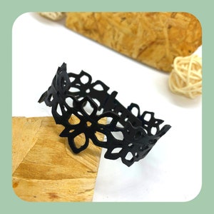 Peut inclure: Bracelet en cuir noir avec un délicat motif floral découpé. Le bracelet est fait d'une seule pièce de cuir qui a été découpée et façonnée pour créer le motif floral.