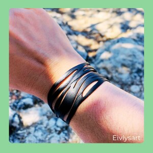 Pode incluir: Pulseira de couro preta com um design ondulado recortado. A pulseira é usada no pulso.