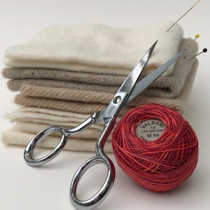 Puede incluir: Una pila de cuadrados de tela beige y blanca con un par de tijeras plateadas y una bola de hilo de bordar roja con el texto "VALDANI 12 COLORFAST M 66".