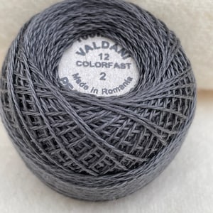 May include: A ball of dark gray embroidery floss with a white label that reads "Valdani 12 Colorfast 2 Made in Romania".