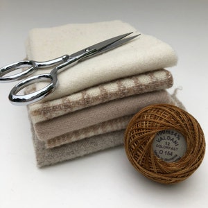 Può includere: Un mucchio di quadrati di tessuto beige e bianco con un paio di forbici d'argento e un gomitolo di lana marrone con un'etichetta che recita "100m+4% VALDANI 12 COLORFAST 0 154 Made in Romania EU"