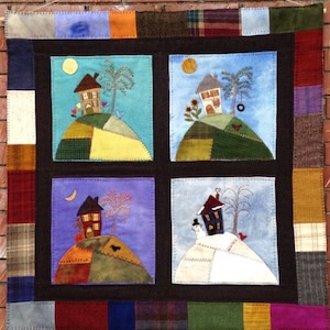 May include: A quilted wall hanging featuring four squares, each depicting a house on a hill in a different season. The top left square shows a house with a yellow sun and green trees. The top right square shows a house with a yellow sun and a green tree. The bottom left square shows a house with a crescent moon and a brown tree. The bottom right square shows a house with a red roof and a white snowman.