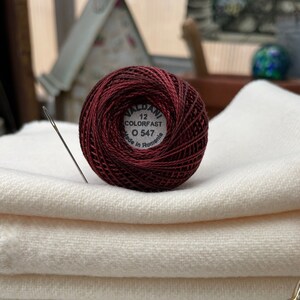 Può includere: Un'bobina di filo da ricamo color borgogna con l'etichetta "VALDANI 12 COLORFAST 0 547 Made in Romania".
