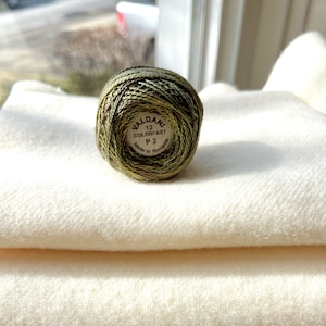 May include: A green, brown, and gold embroidery floss spool with the label "VALDANI 12 COLORFAST P2 Made in Romania".