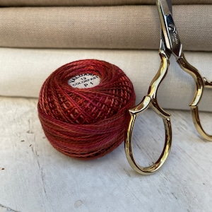 May include: A ball of red and orange embroidery floss with a white label that reads "12 COLORFAST P1" and a pair of gold scissors.