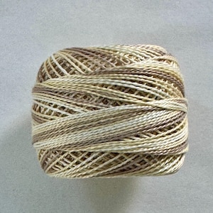 May include: A ball of variegated yarn in shades of beige, brown, and cream. The yarn is tightly wound, showing the texture of the individual strands. Ideal for knitting, crocheting, or other fiber arts projects.