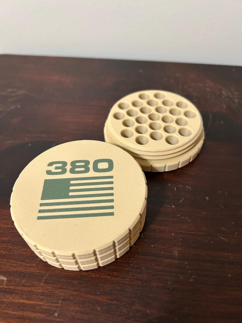 May include: Tan-colored round container with the number "380" and a green flag design. The container is open, revealing a grid of small holes. The container is made of a ridged material.