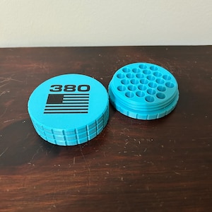 May include: Two-piece, light blue container with the number "380" and a black graphic. The container is cylindrical with a ridged edge. The second piece has multiple holes. The items are on a dark wooden surface.