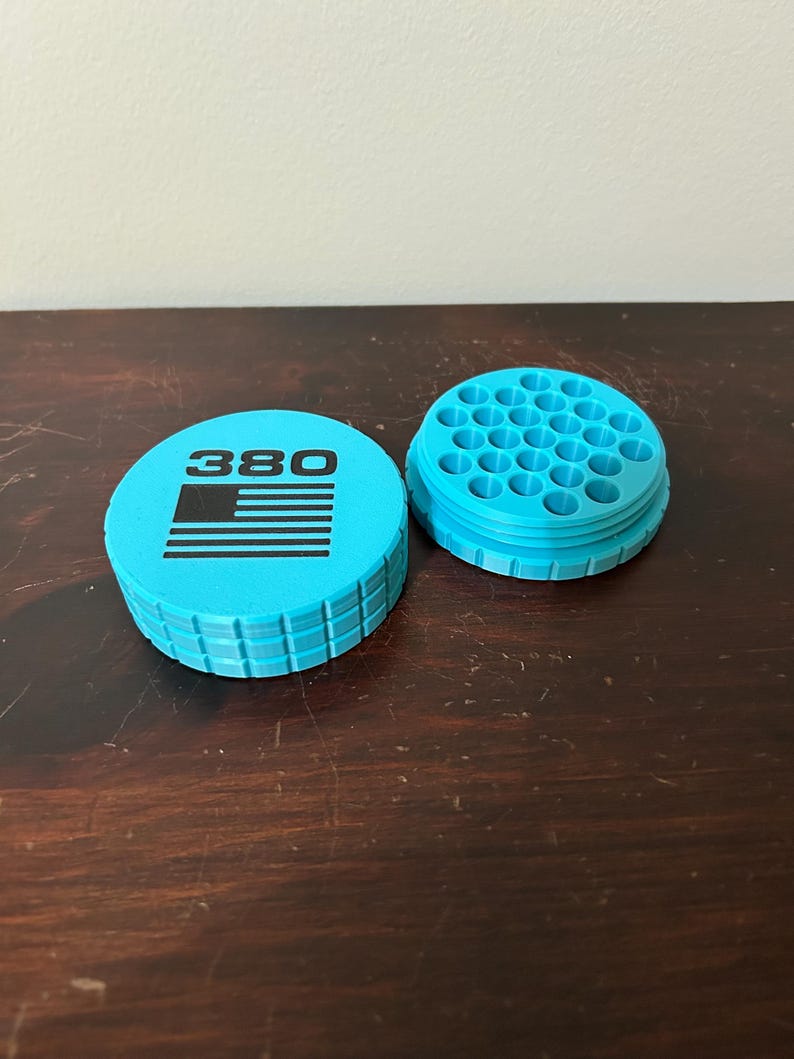 May include: Two-piece, light blue container with the number "380" and a black graphic. The container is cylindrical with a ridged edge. The second piece has multiple holes. The items are on a dark wooden surface.