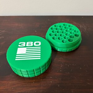 May include: A green, circular container with the number "380" and a white American flag design on the lid. The container is open, revealing a grid of small holes. The item is made of plastic.