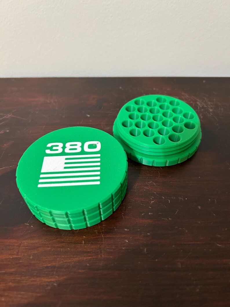 May include: A green, circular container with the number "380" and a white American flag design on the lid. The container is open, revealing a grid of small holes. The item is made of plastic.