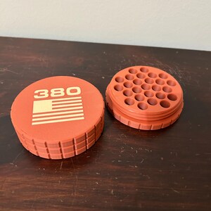May include: An orange container with the number "380" and a striped design on the lid. The container is open, revealing multiple holes. The container is made of a textured material.