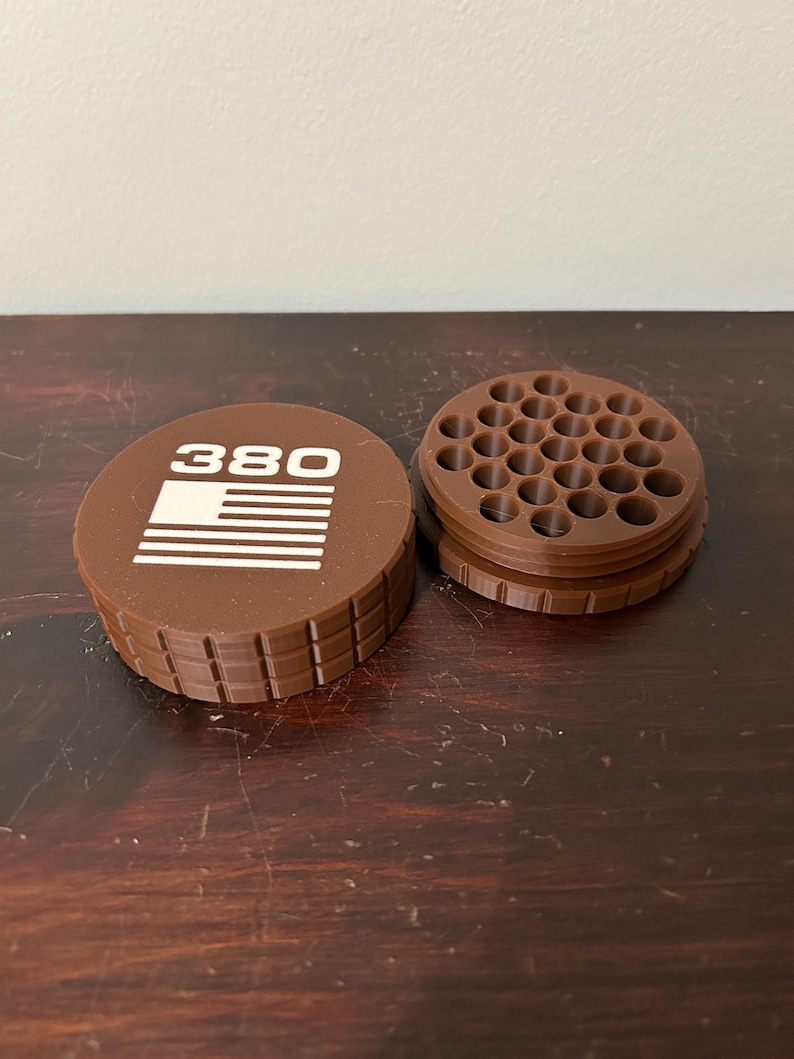 May include: A brown, 3D-printed container with a lid featuring the number "380" and a white graphic. The container is open, revealing a grid of small holes. The design is likely for organizing small items.