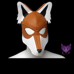 May include: A handcrafted fox mask made of brown, white, and black leather. The mask features a detailed fox face with pointed ears, eye openings, and a snout. The mask is designed to be worn and is displayed on a white form.