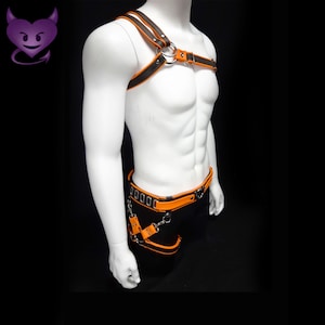 May include: A black and orange leather harness with silver hardware. The harness has a chest strap, a waist strap, and a thigh strap. The harness is worn on a mannequin.