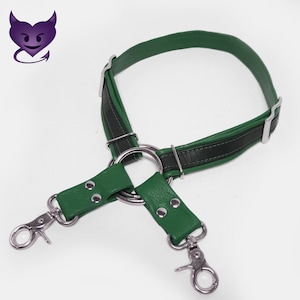 May include: A green leather harness with two metal clips and a large metal ring. The harness is made of two pieces of leather that are joined together by the ring.