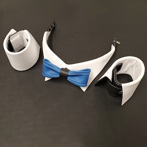 May include: A set of white leather cuffs and a white collar with a blue bow tie. The bow tie is blue with white stitching. The cuffs and collar have black accents.