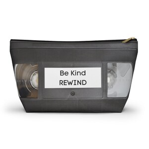 May include: A black and gray VHS tape-style zippered pouch with the text "Be Kind REWIND" on a white label.