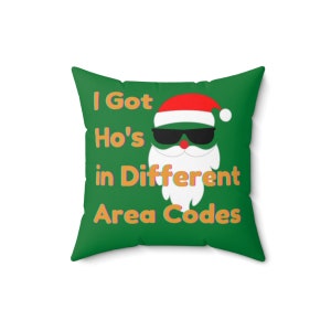 May include: Green throw pillow with a white Santa Claus wearing sunglasses and a red hat. The text on the pillow reads "I Got Ho's in Different Area Codes".