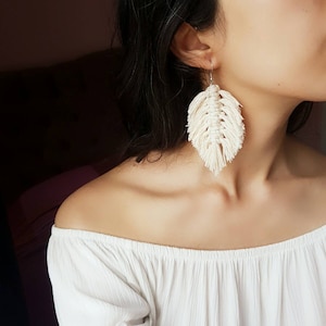 May include: A pair of white feather-shaped earrings made with macrame knotting.