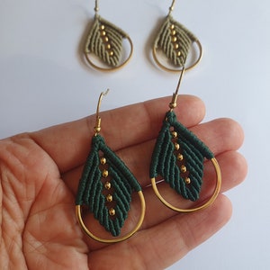 May include: A pair of green and gold earrings with a leaf design. The earrings are made with a macrame technique and have gold hoops.