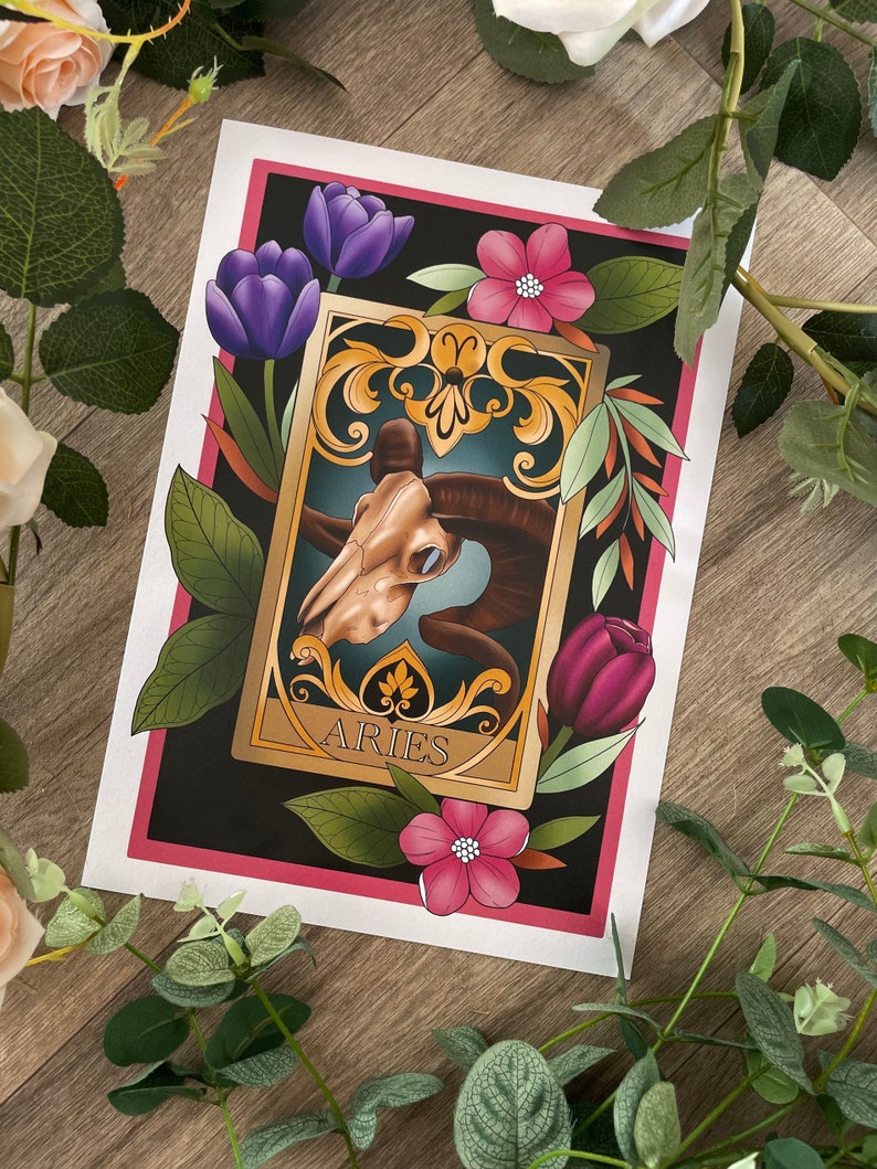 May include: A vintage-style illustration of the zodiac sign Aries. The image features a ram skull with ornate gold details and floral accents in shades of pink, purple, and green. The text "Aries" is written in gold lettering.