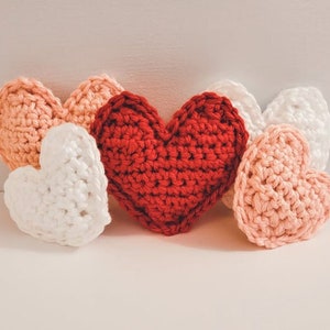 A set of small and large crochet hearts made of bulky yarn against a white backdrop. There are two pink, two white and one red heart.