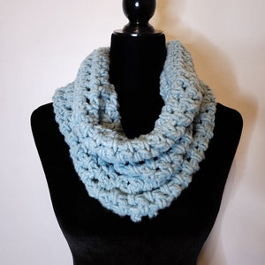 A light blue crochet fleece cowl displayed on a black velvet mannequin against a white backdrop.