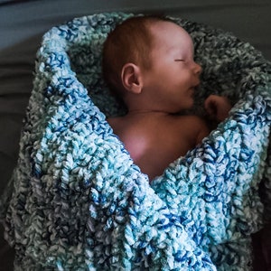 May include: A newborn baby sleeping peacefully in a blue and white fuzzy blanket.