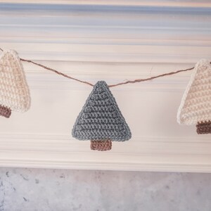 Crocheted Christmas Trees strung into a garland draped across a white mantle with jute. The trees are made of green and cream yarn with light brown trunks.