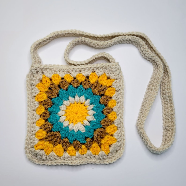 A yellow, cream, caramel and blue crochet granny square bag on a white background.