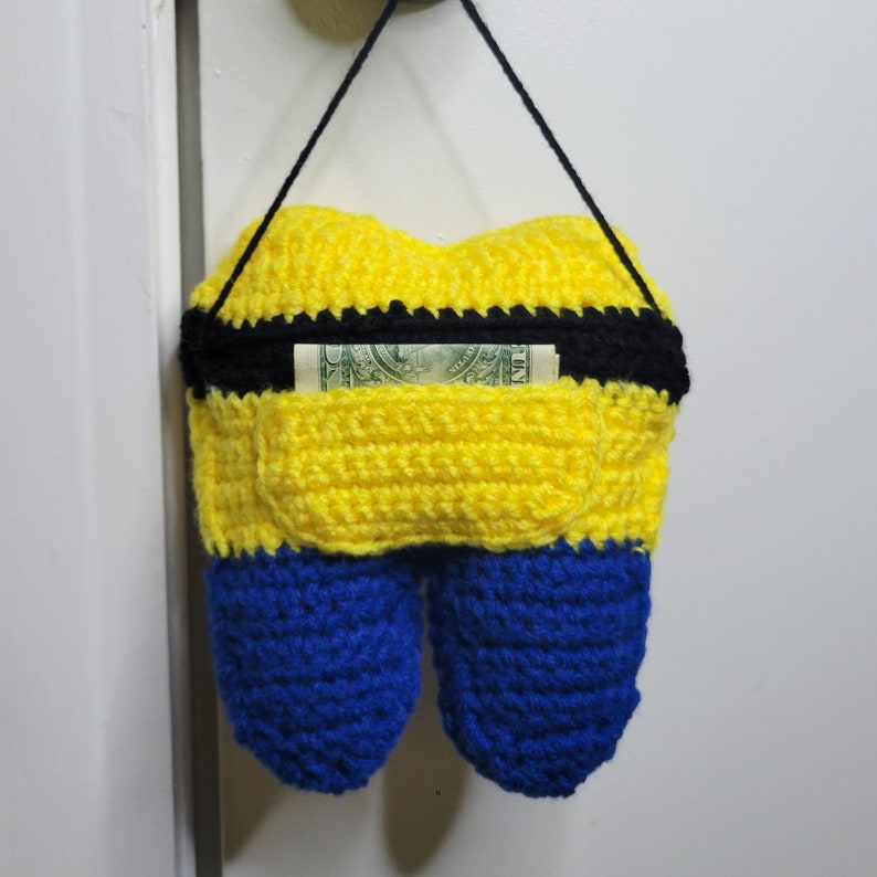 Back image of the Crochet Tooth Fairy Pillow - Yellow guy hanging on a door knob with a dollar in the tooth pocket.