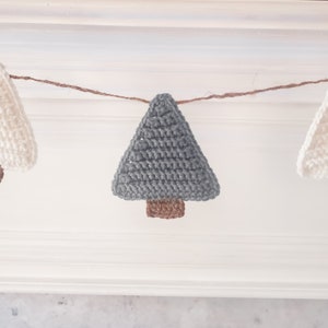 Crocheted Christmas Trees strung into a garland draped across a white mantle with jute. The trees are made of green and cream yarn with light brown trunks.