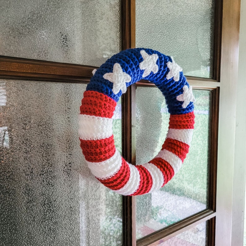Crochet American Flag Wreath hanging on a glass and wooden door. The yarn is red, white and blue.