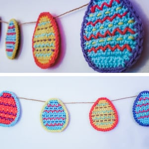 Puede incluir: Una guirnalda de huevos de Pascua de ganchillo en varios colores y patrones, incluyendo azul, amarillo, rojo y morado. Los huevos están unidos con un cordel y cuelgan de una pared blanca.