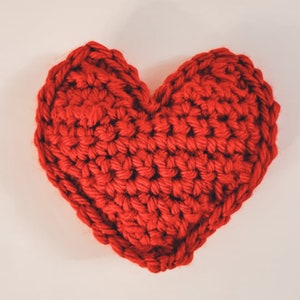 One close up of a large red crochet heart plushie. You can see each crochet stitch made with the chunky yarn.