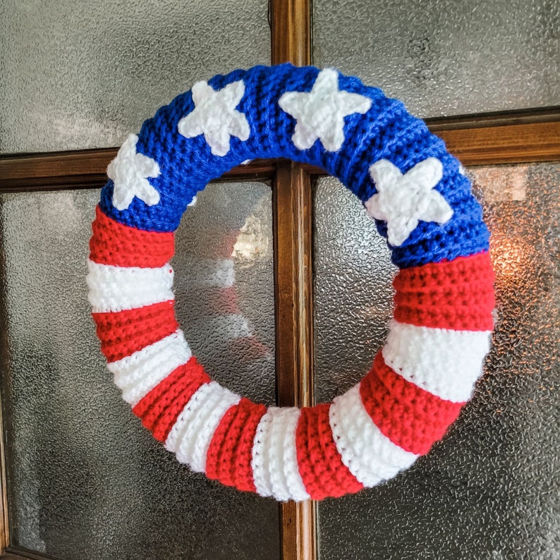 Crochet American Flag Wreath hanging on a glass and wooden door. The yarn is red, white and blue.