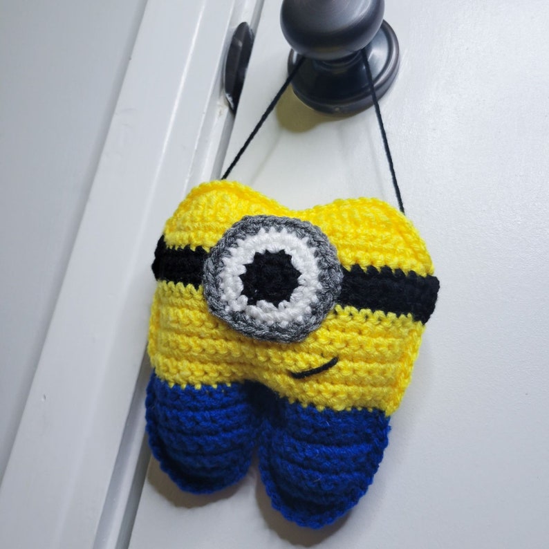 Front image of the Crochet Tooth Fairy Pillow - Yellow guy hanging on a door knob.