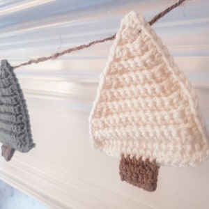 Crocheted Christmas Trees strung into a garland draped across a white mantle with jute. The trees are made of green and cream yarn with light brown trunks.