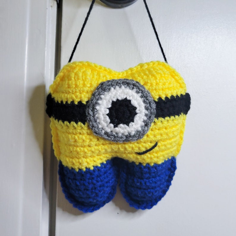 Front image of the Crochet Tooth Fairy Pillow - Yellow guy hanging on a door knob.