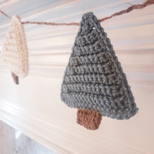 Crocheted Christmas Trees strung into a garland draped across a white mantle with jute. The trees are made of green and cream yarn with light brown trunks.