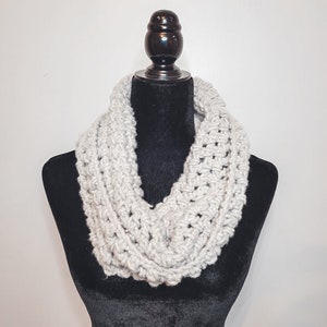 A light grey crochet fleece cowl displayed on a black velvet mannequin against a white backdrop.