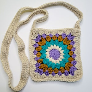 A purple, cream, caramel and blue crochet granny square bag on a white background.