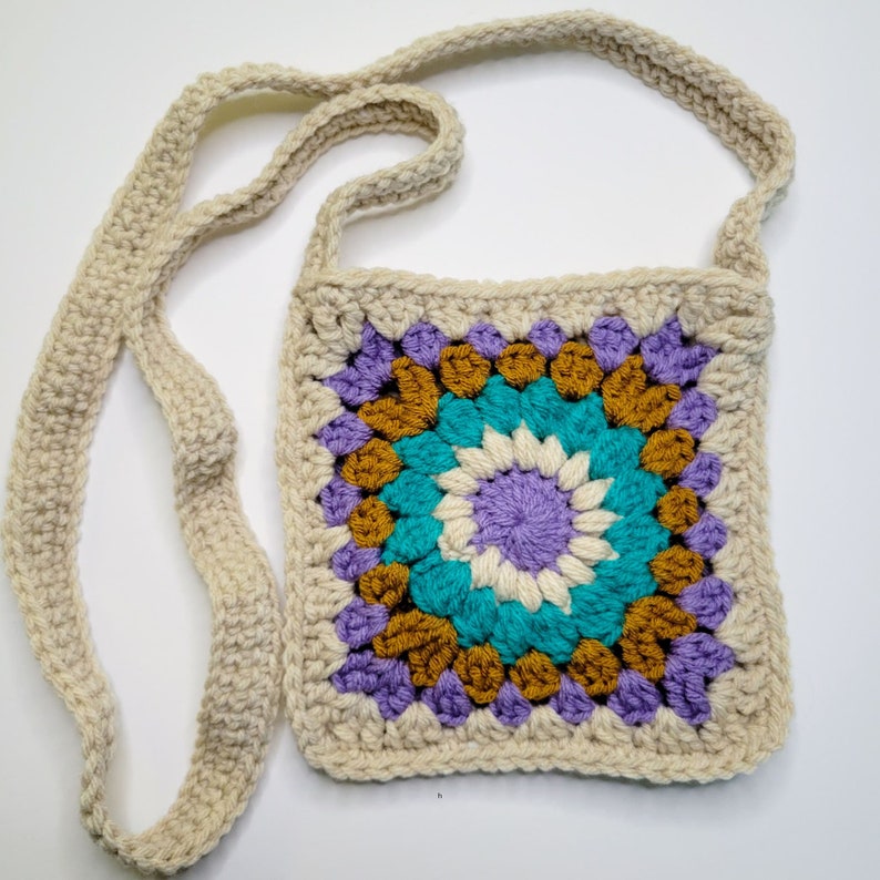 A purple, cream, caramel and blue crochet granny square bag on a white background.