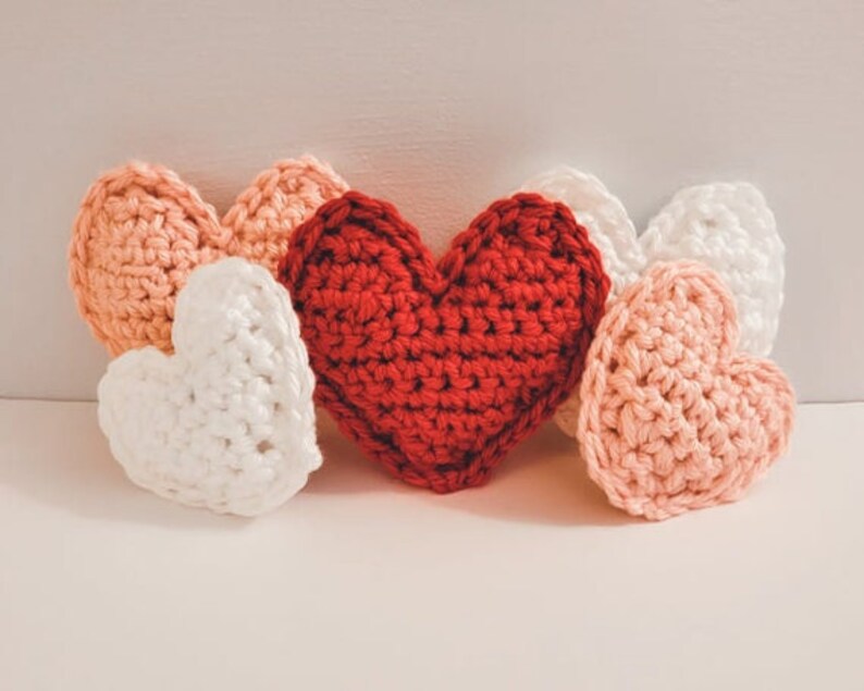 A set of small and large crochet hearts made of bulky yarn against a white backdrop. There are two pink, two white and one red heart.