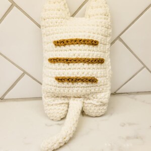 The backside view of the crochet kitty cat against a white background displaying three caramel colored stripes on the kitty's back.